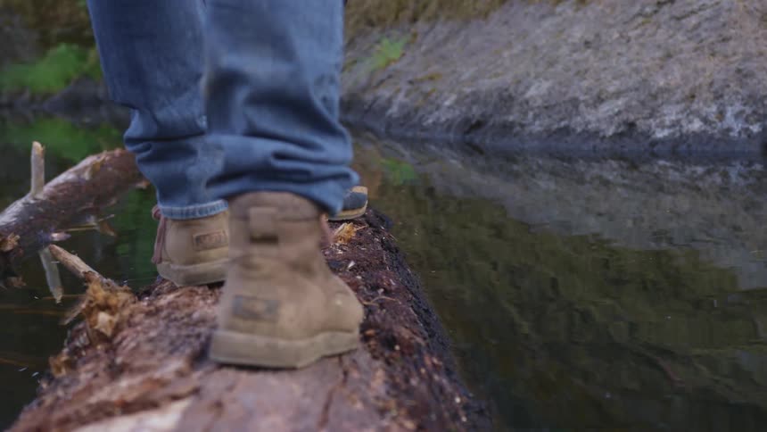 People walking and one jumping off a log on a creek