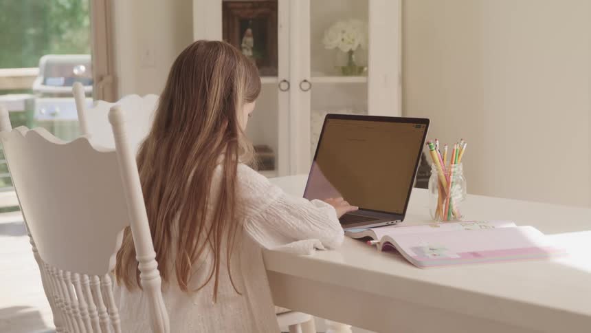 A young girl with long hair doing homework on a laptop at home