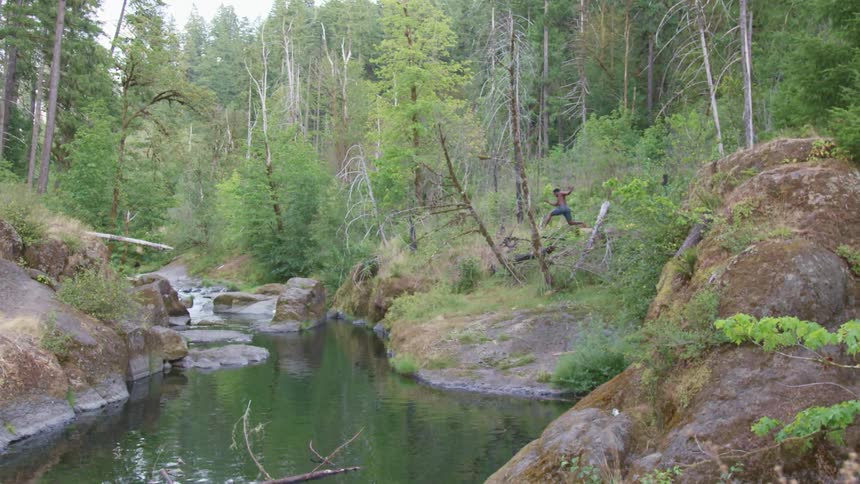 Man wearing shorts jumps from top of promontory into water in forest
