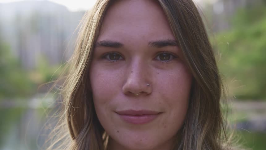 A young woman smiles into the camera while standing outdoors during the day
