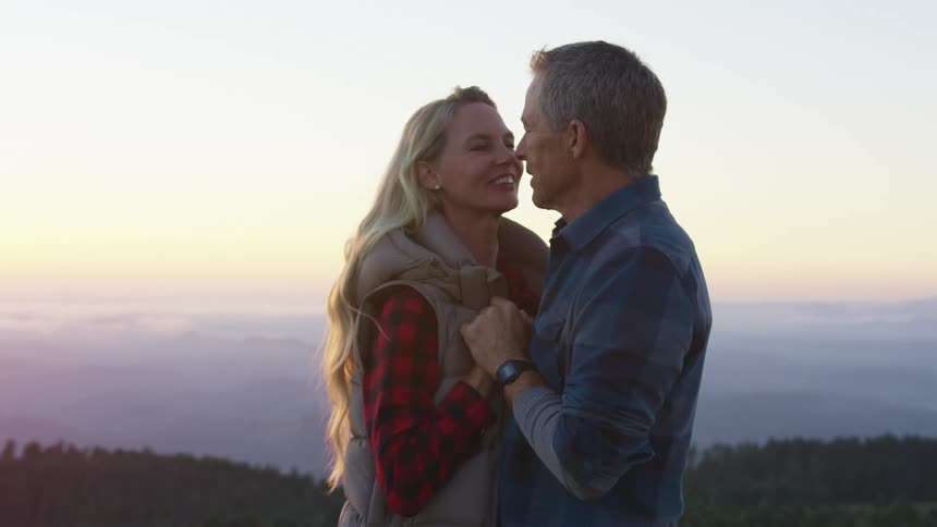 A man and a woman smile at one another while dancing at an elevated point overlooking a natural landscape