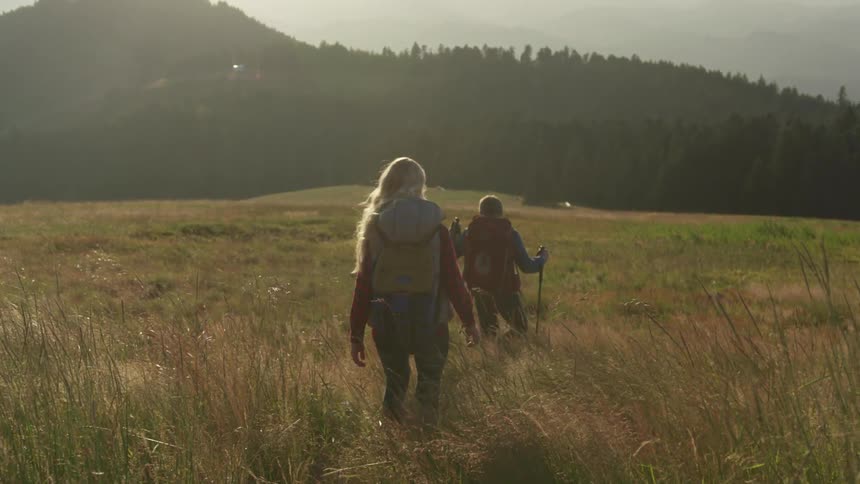 A man and woman hiking across a grassy field in nature