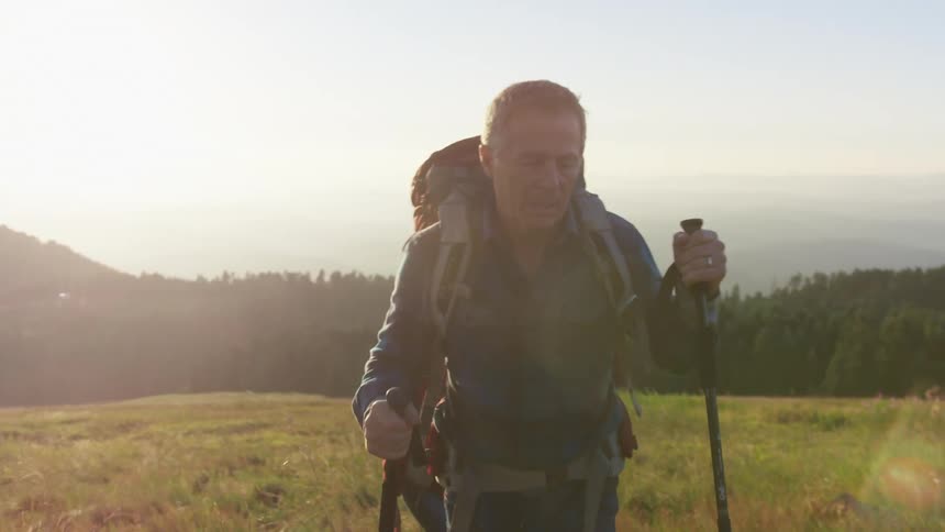 A man and woman hiking across a grassy field in nature on a sunny day