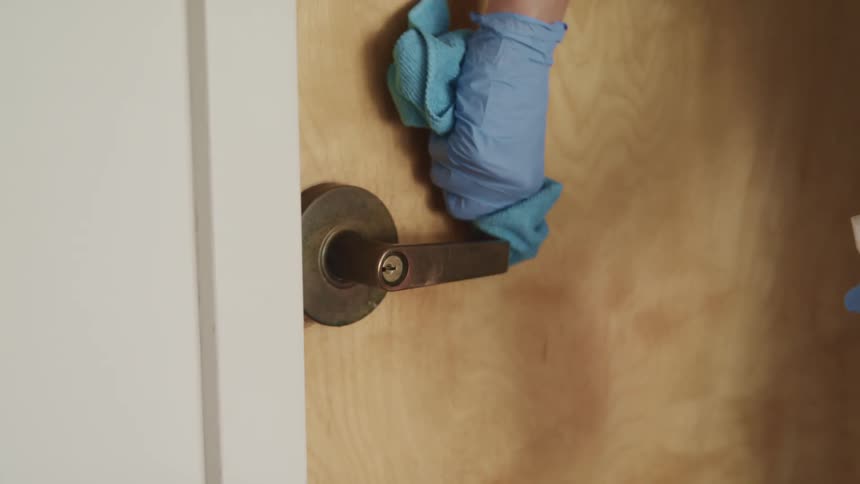 A person with gloved hand washing a door handle