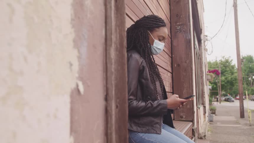 A woman leans against a city building looking at her cell phone