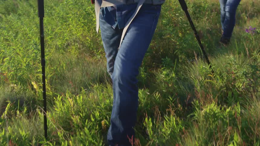 Two people with jeans and boots walking on a grassy hill