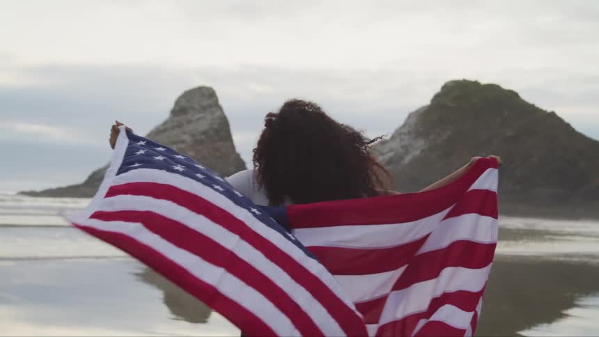 A girl is running across a beach carrying an american flag behind her