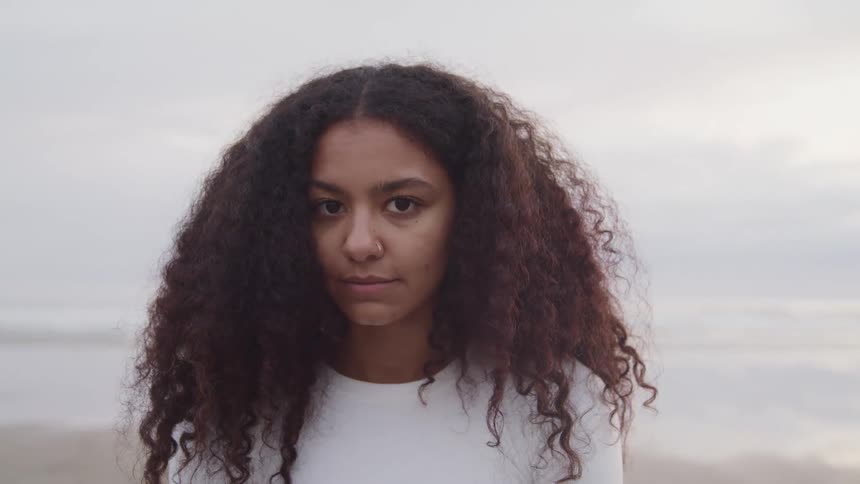 Young long haired woman standing on a beach looks up at the camera
