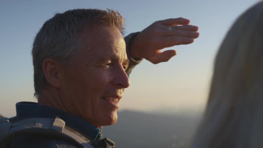 Senior citizen shielding his eyes from the sunset sunlight while talking to a woman