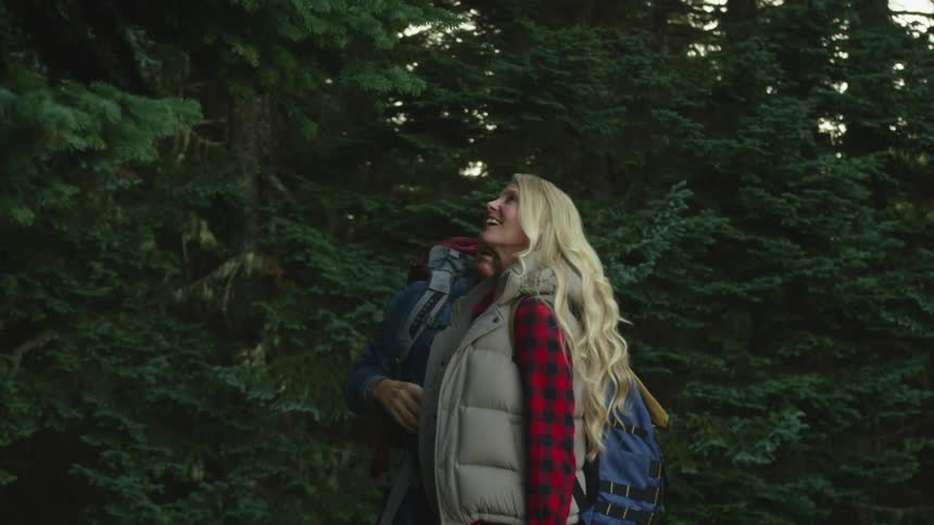 A man and a woman with backpacks in a forest with trees
