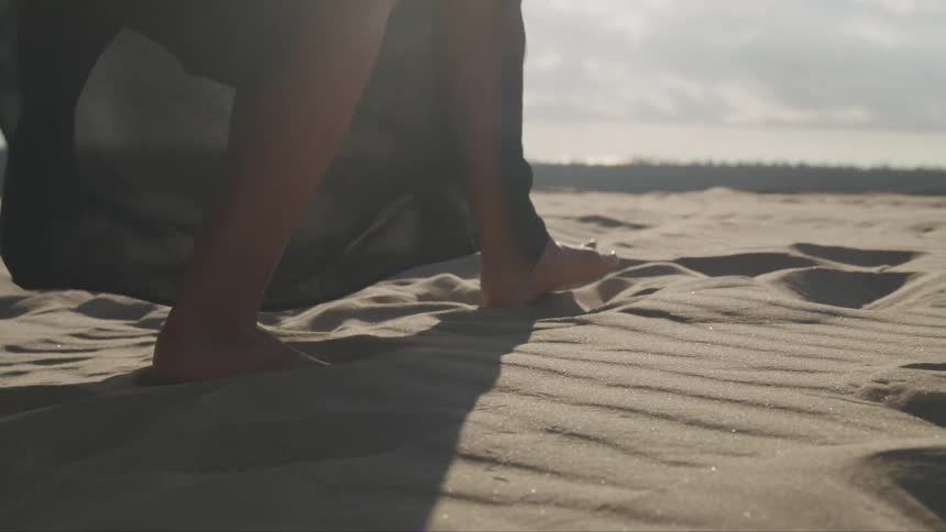 A woman with a dress walking on sand with the sky and clouds in the background