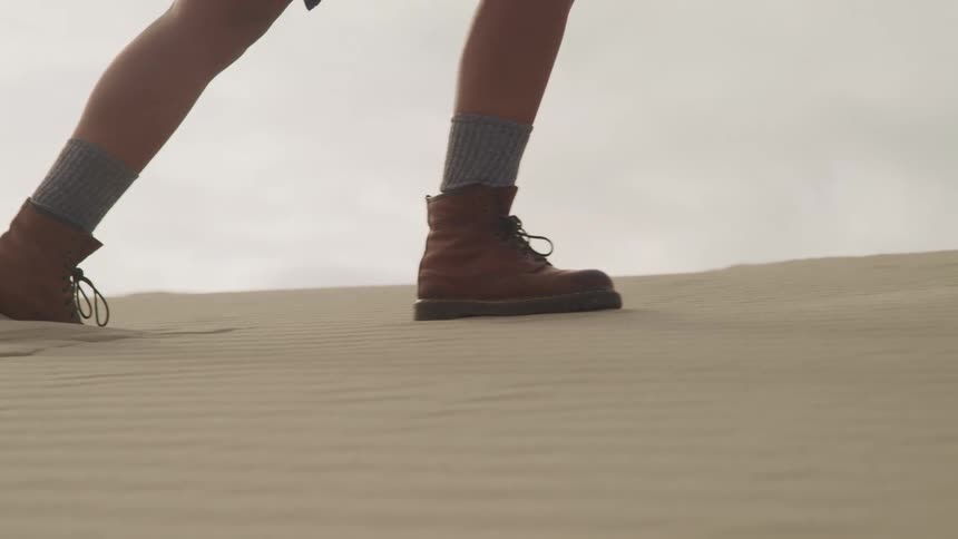 Person wearing hiking boots walks across sand under cloudy sky