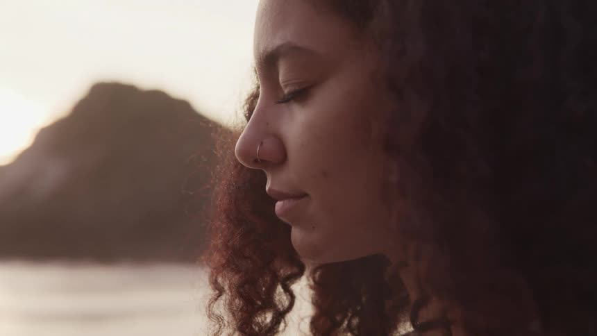 A woman with a nose ring outside on a beach with her eyes closed