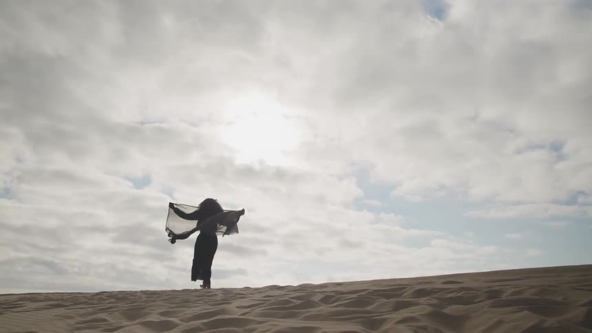 A woman in a black gown walks in the sand