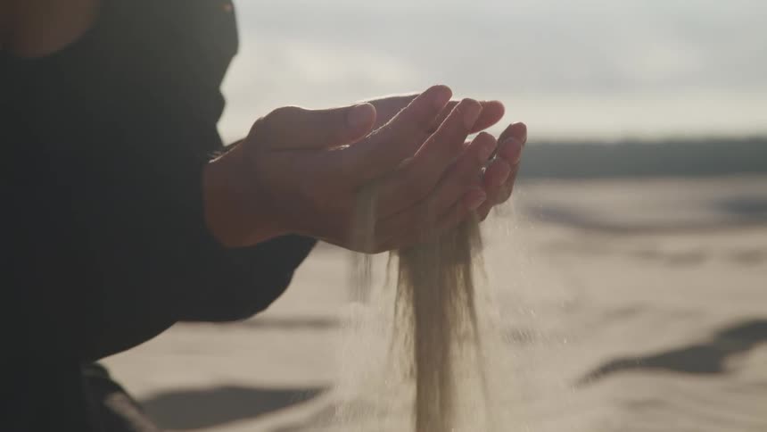 Sand sifting through a persons hands outside in the daytime
