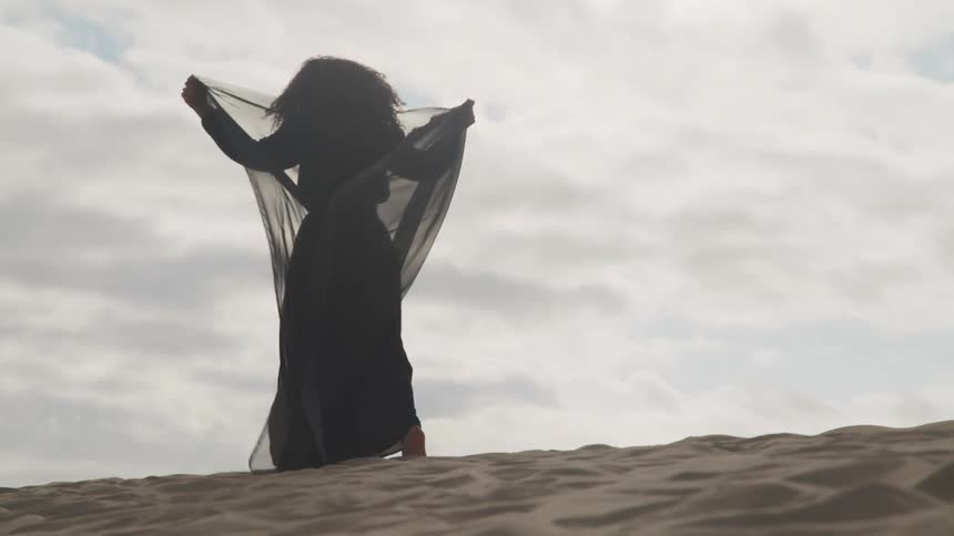 A woman is wearing a dress and walking on the beach