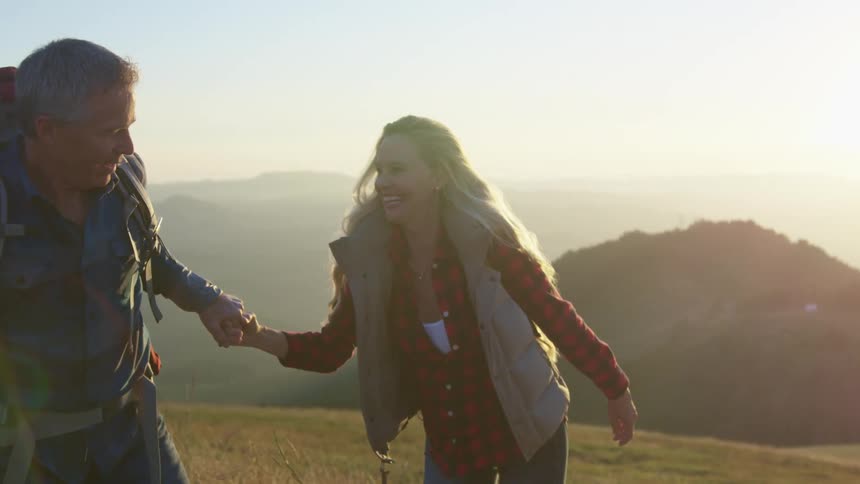 Mature couple hiking on the slopes of a mountainside at sunset