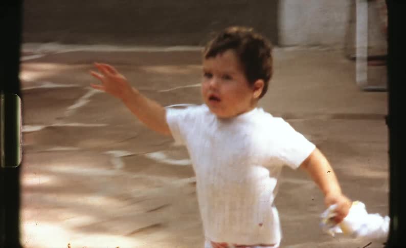 A little boy running up to a woman as she picks him up with a house and chairs in the background