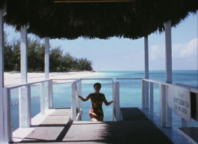 A woman in a swimsuit climbs the stairs onto a platform on a beach on a sunny day
