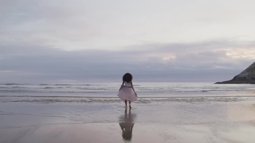 A woman stands on the beach by herself and spins with a shaw behind her in the wind
