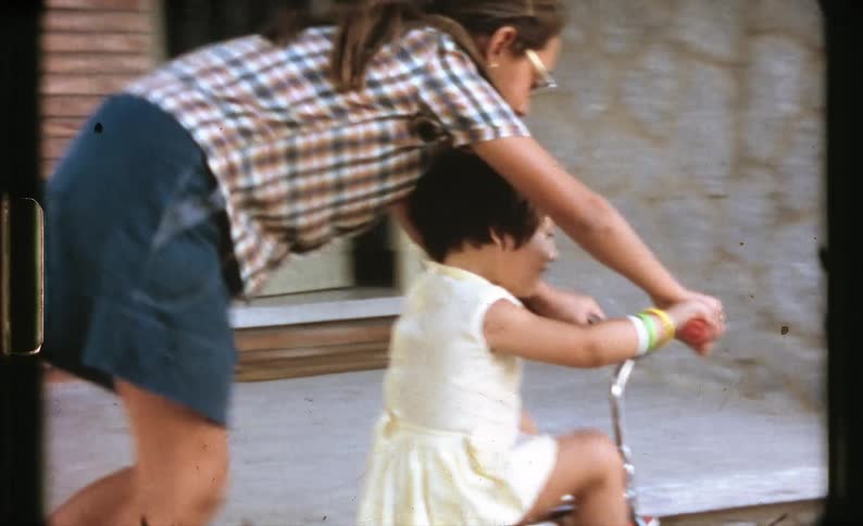 A girl is teaching her sister how to ride a bike