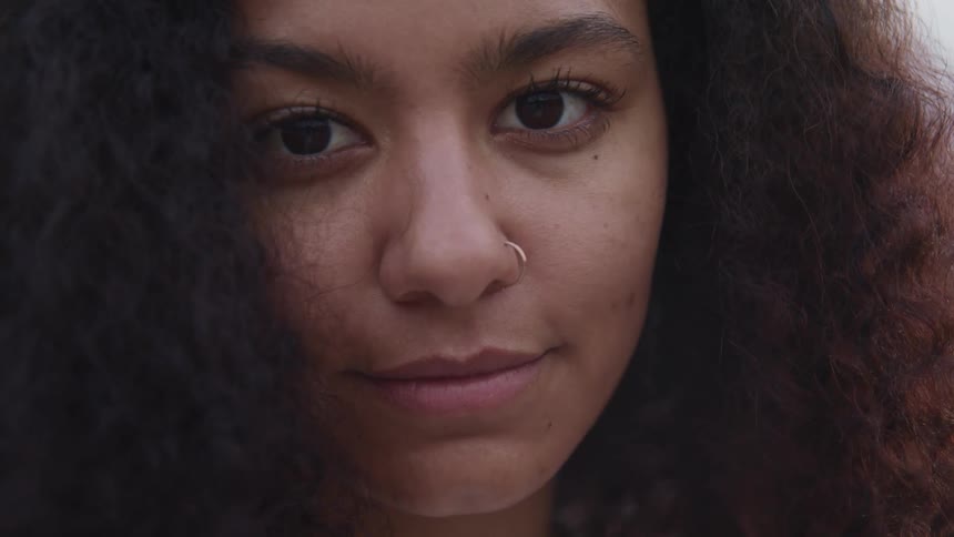 Woman with frizzy hair and nose ring faces the camera with eye contact