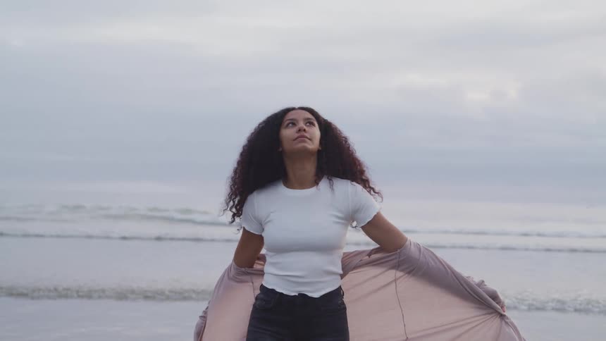 A woman is spinning around on the beach