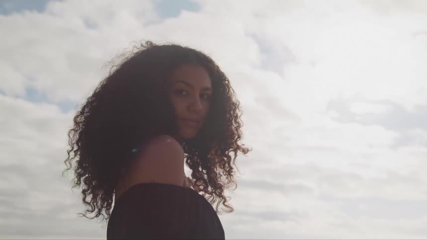 A woman standing and staring with the sky and clouds in the background