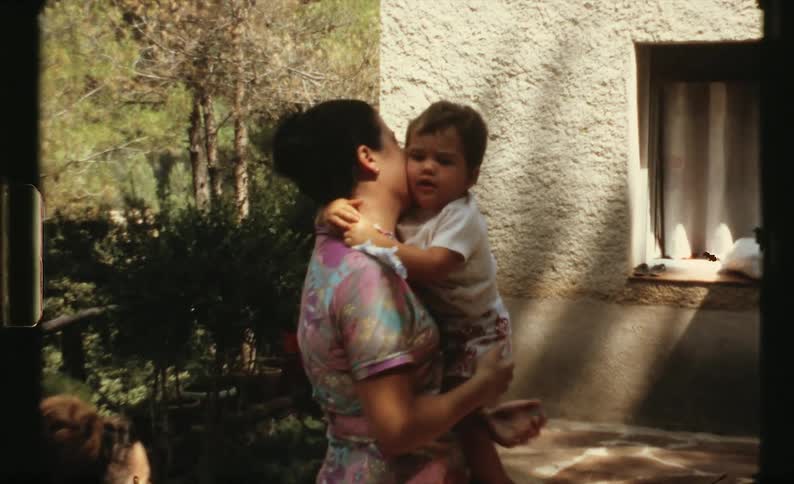 Mother hugs and kisses child standing next to house
