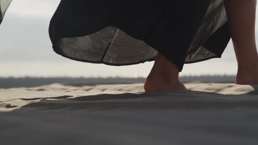 Woman wearing filmy black fabric walks across sand