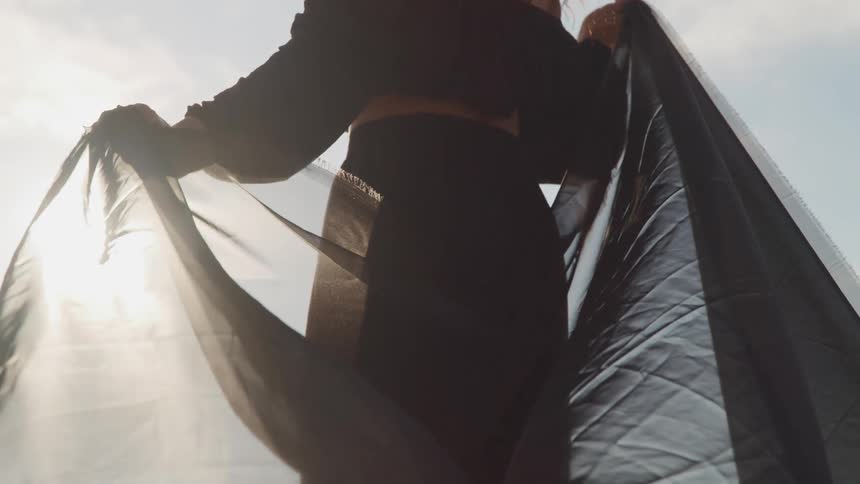 Sunlight filtering through a black piece of cloth in the hands of a woman standing outdoors