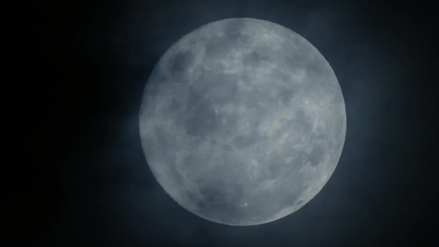 Clouds passing in front of the glowing moon at night