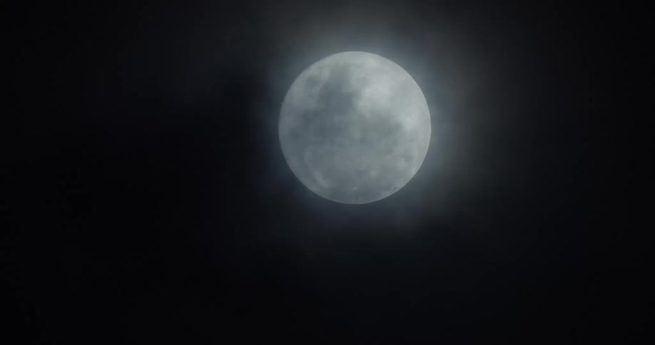 Clouds pass over full moon shining at night