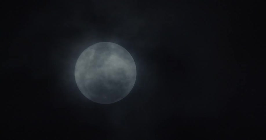 Dark clouds flow across face of full moon at night