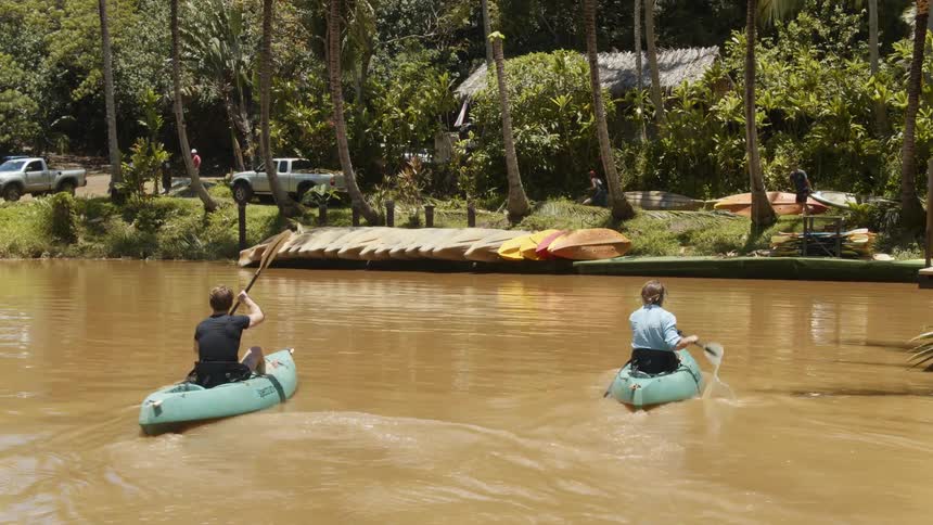 Two men kayak on a river on a sunny day