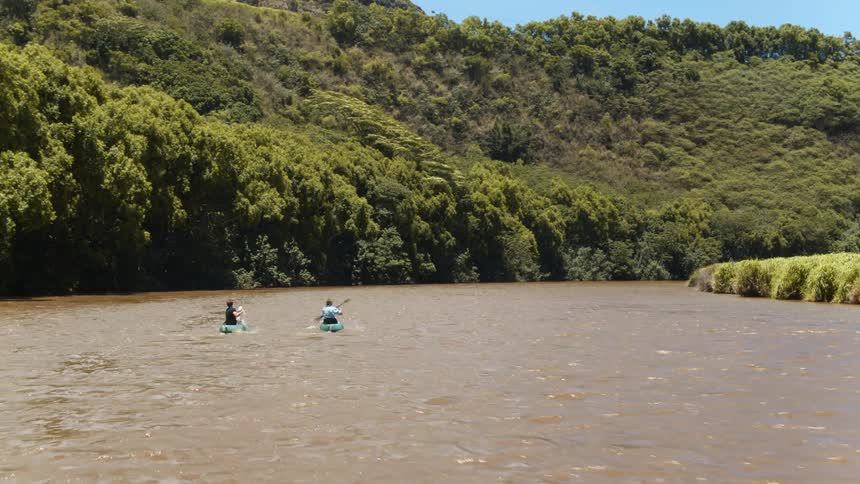 Two people each paddle a canoe in a river