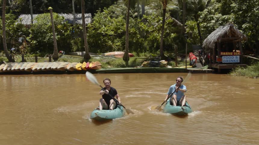 Two men paddle boats on the brown water