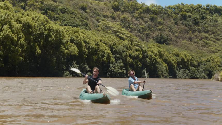 Two men kayak on a river on a sunny day