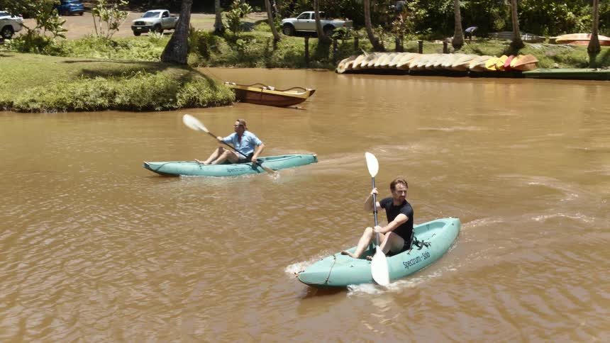 Two men kayak on a river on a sunny day