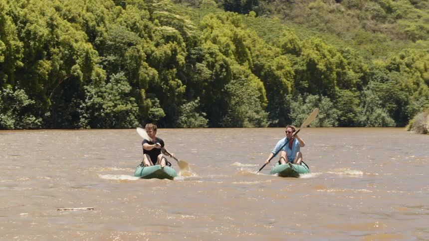 Two men kayak on a river on a sunny day