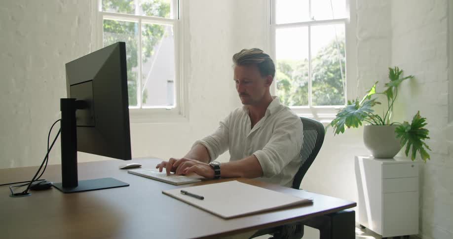 Man typing on computer keyboard studies monitor while sitting in home office