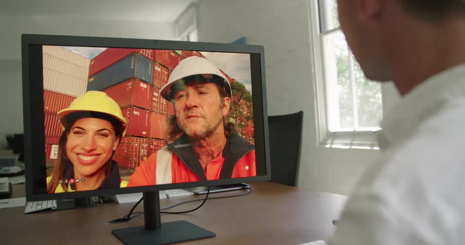 Two workers standing near shipping containers video conference with worker in office