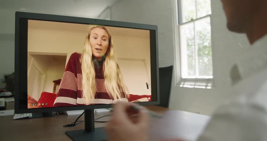 A man talks with a woman through video chat on a computer while sitting at a table during the day