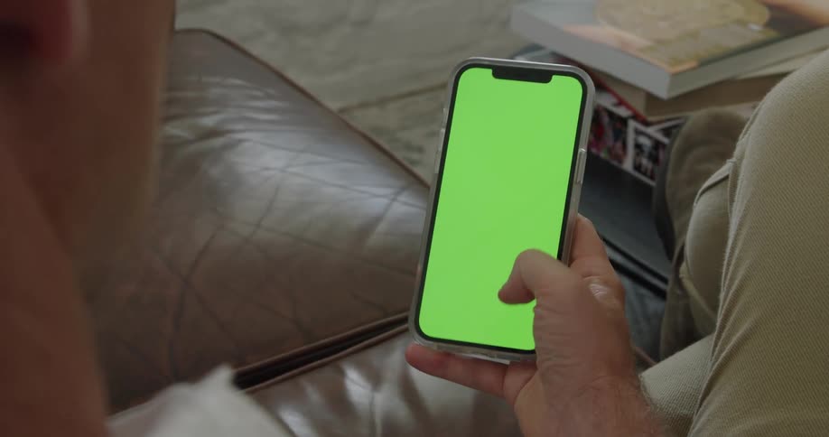 Man sitting on couch scrolls mobile phone with green screen