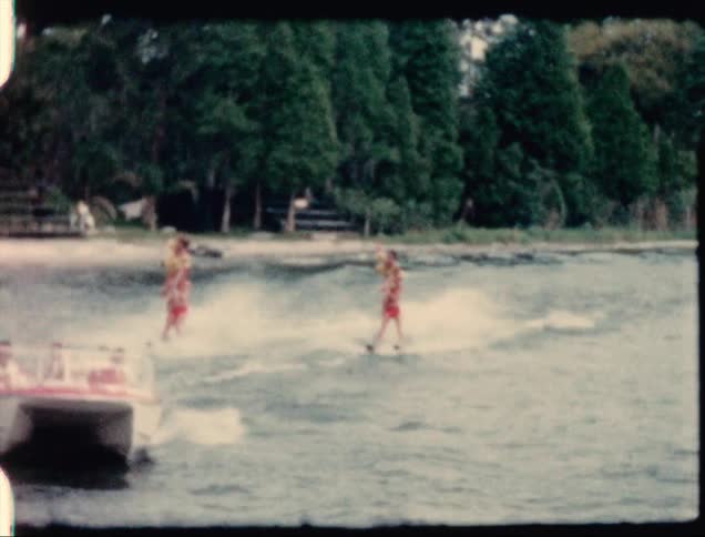 An audience in stands on the beach watches as a boat pulls water skiers doing tricks