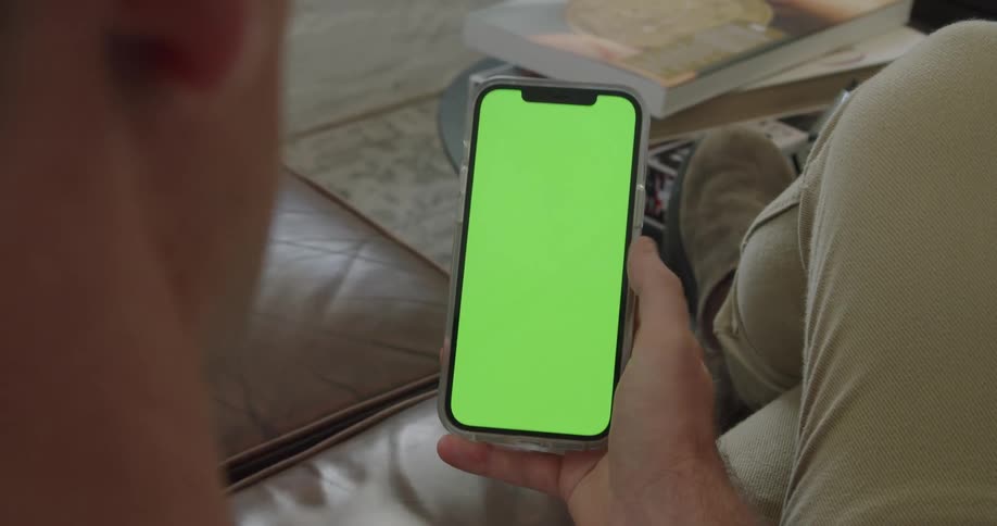 A man scrolls on a green screen on a cell phone