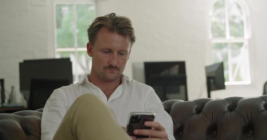 Man sitting on couch near desk views mobile phone