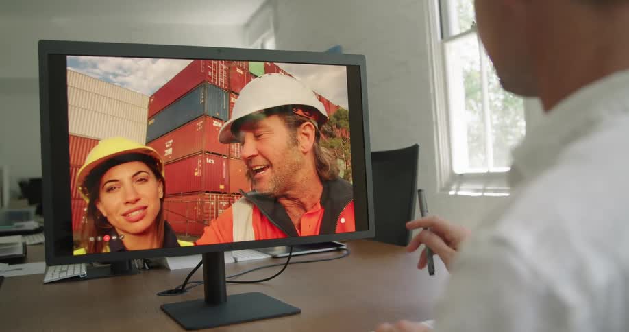 Man sitting at a desk talking to dock workers on a video call in a computer
