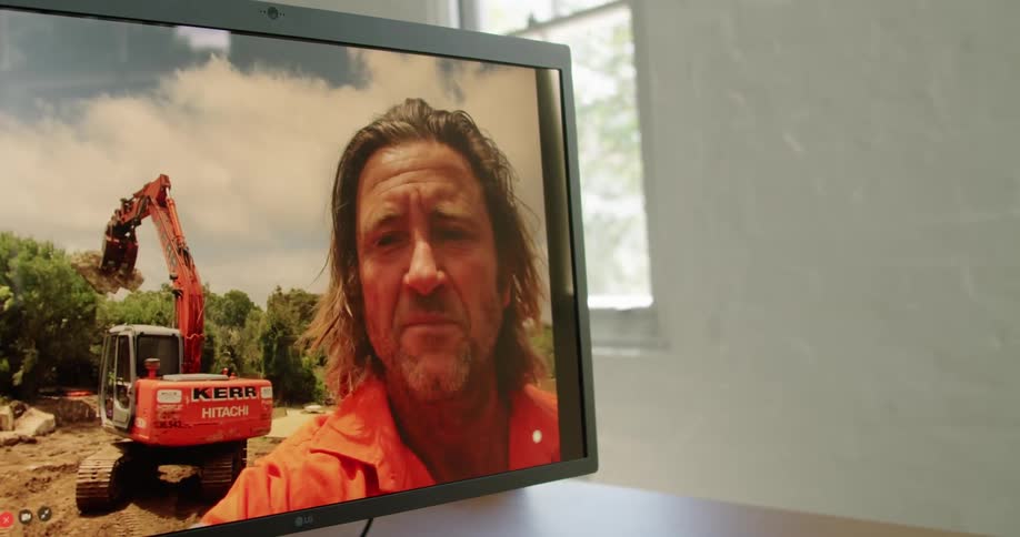 Man sitting at a desk talking to construction workers on a video call in a computer