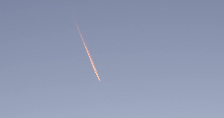 An aircraft flies in the sky leaving a trail behind it